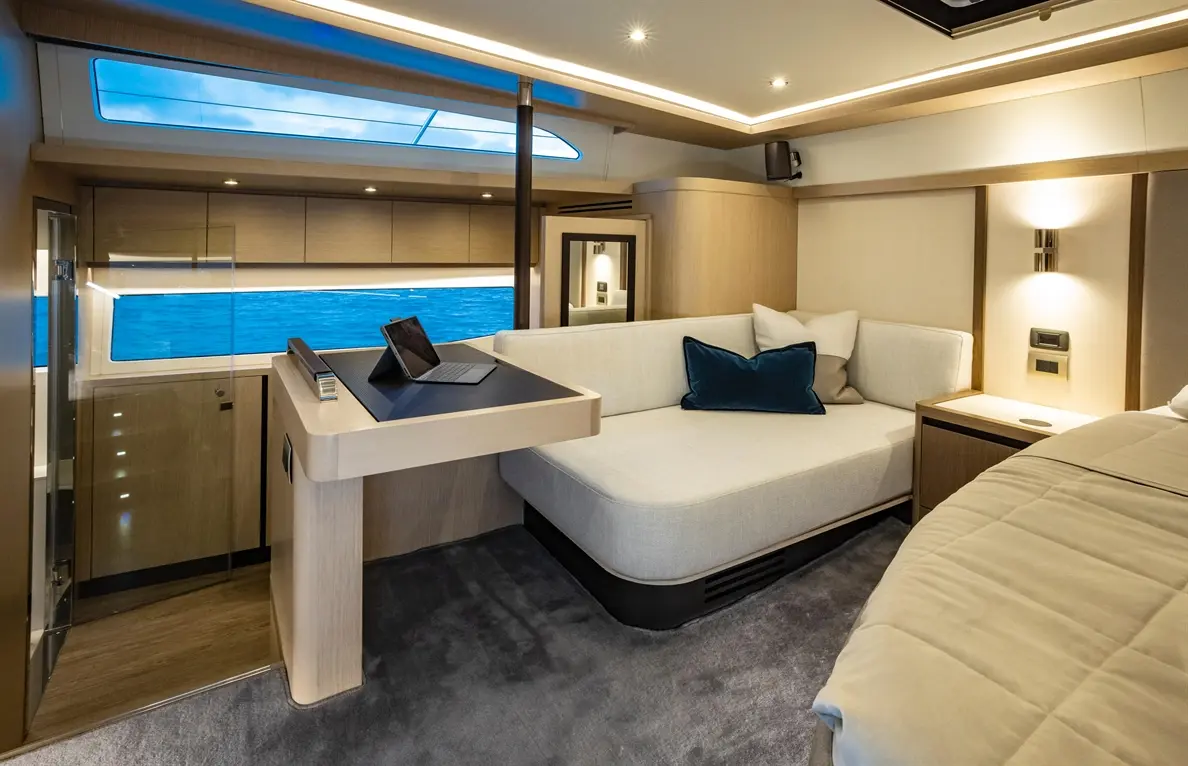 Stylish yacht interior featuring a sofa, workstation with a tablet, and panoramic views of the ocean through large windows.